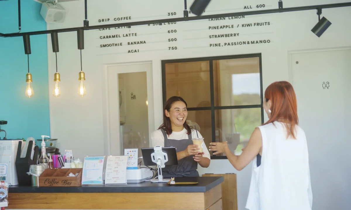 the SCAMPSドッグパーク併設カフェの店内で、スタッフが笑顔でドリンクを手渡している様子